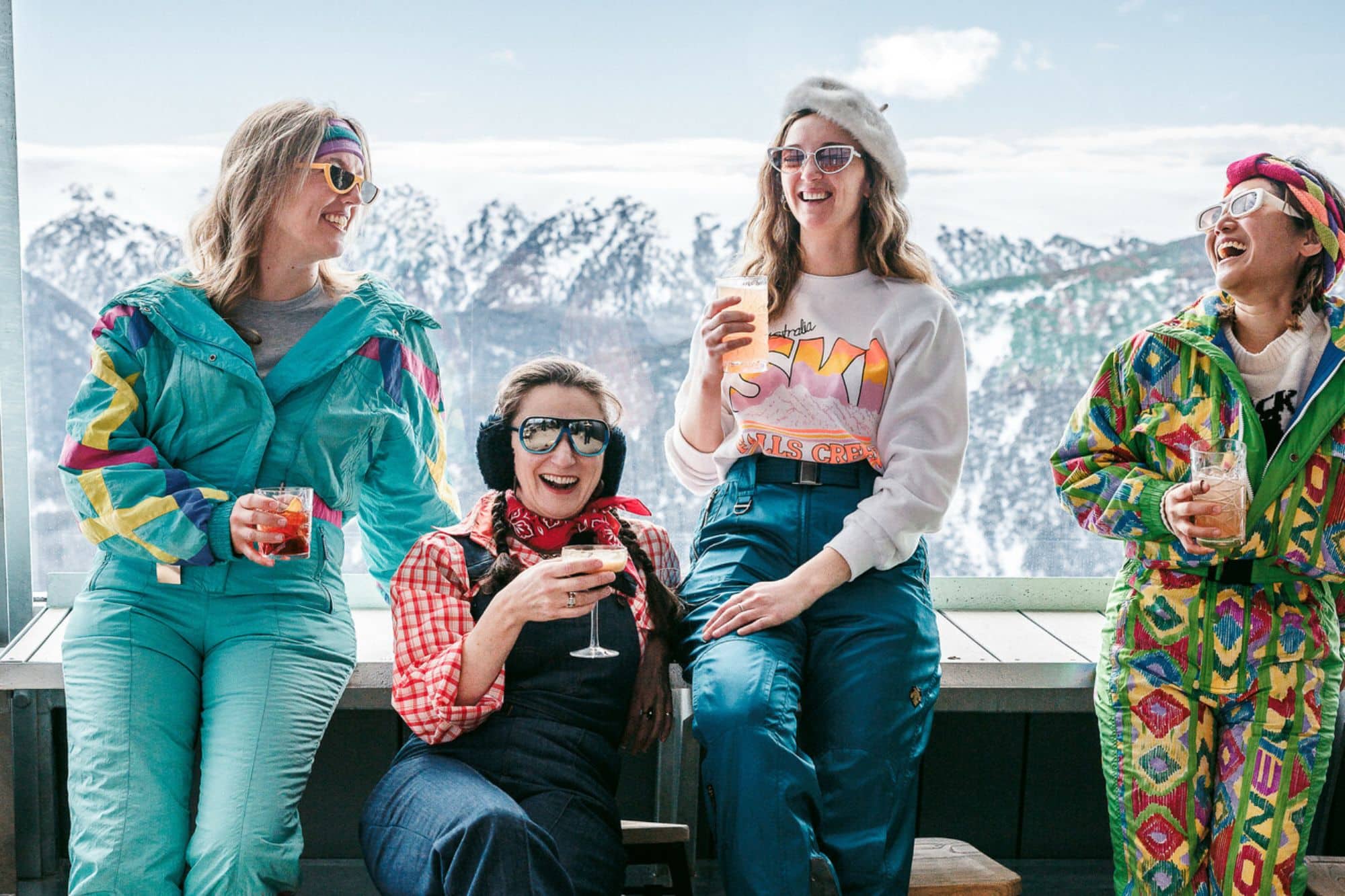 Group of people in vintage snow wear enjoying cocktails at Cloud 9 with snow covered mountain views in the background.