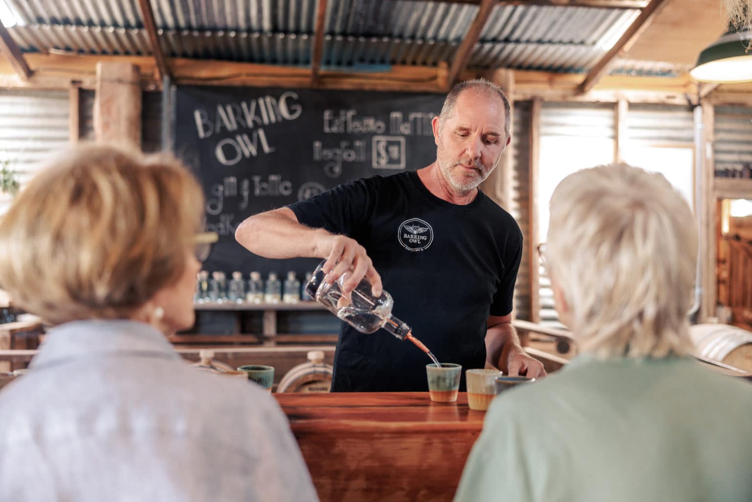 Distiller pouring gin into handmade ceramic cup at Barking Owl Distilery.