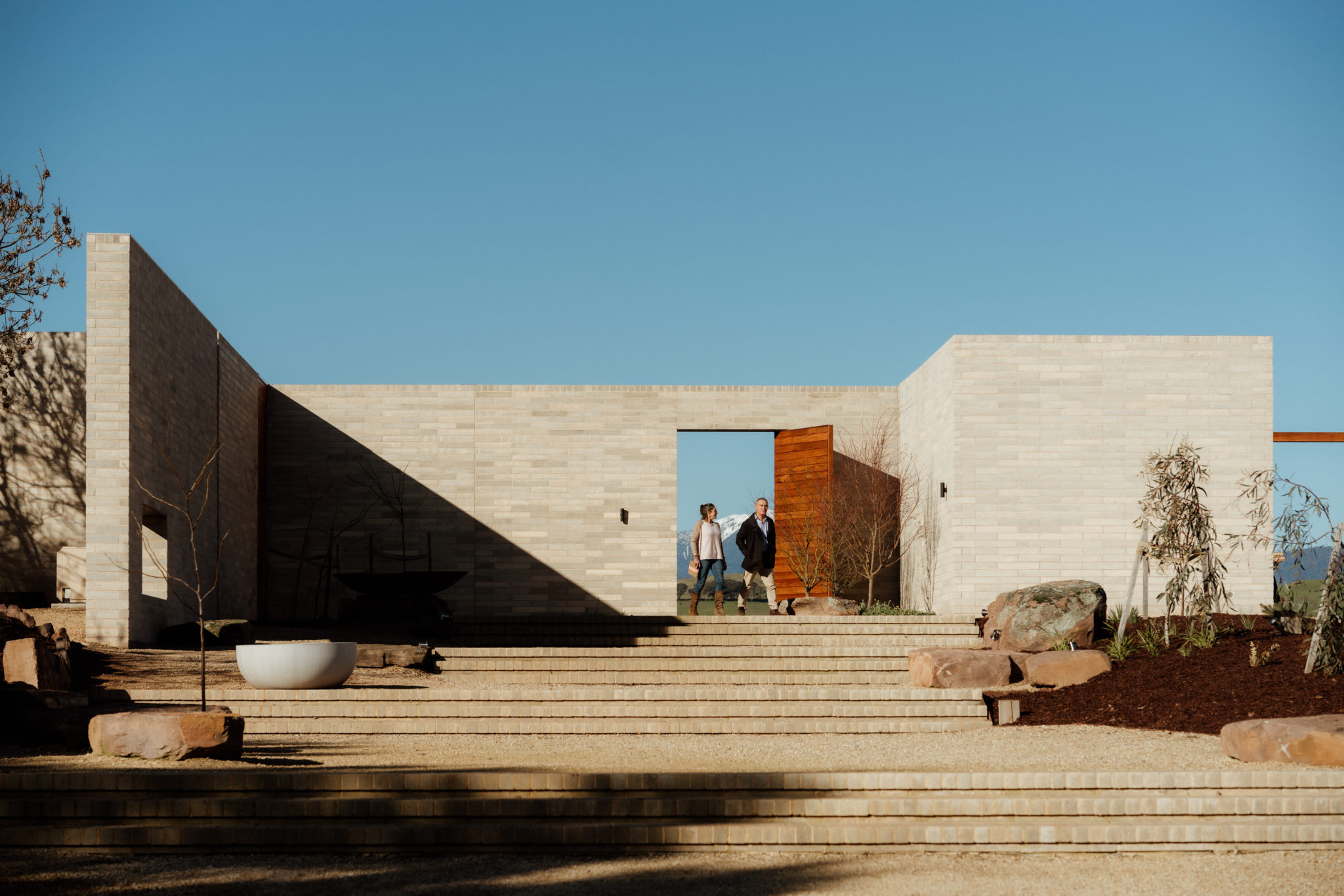 A couple walking at Delatite Winery, with view of Mt Bogong and cellar door feature door