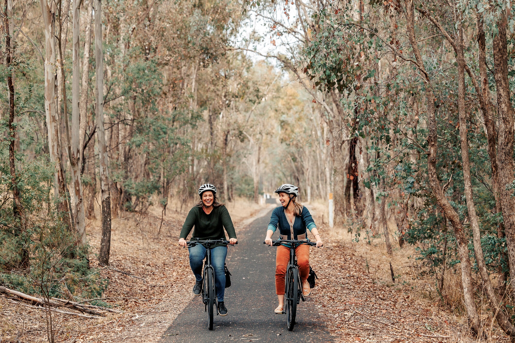 Two riders pedalling and laughing on the Muray to Mountains Rail Trail riding between native trees
