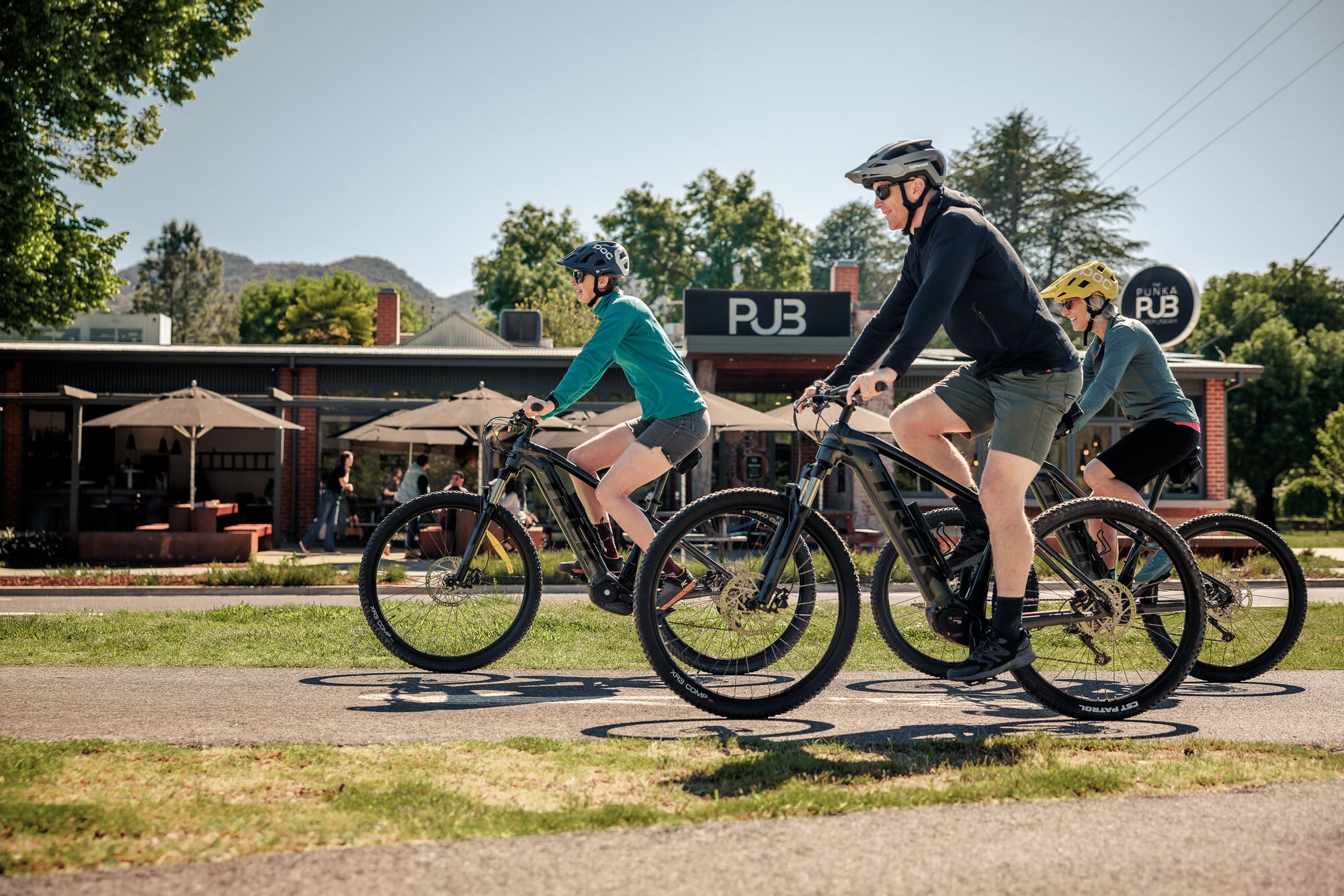 Group of cyclists riding past the Porepunkah Pub on the Murray to Mountains Rail Trail with a blue sky in the background.