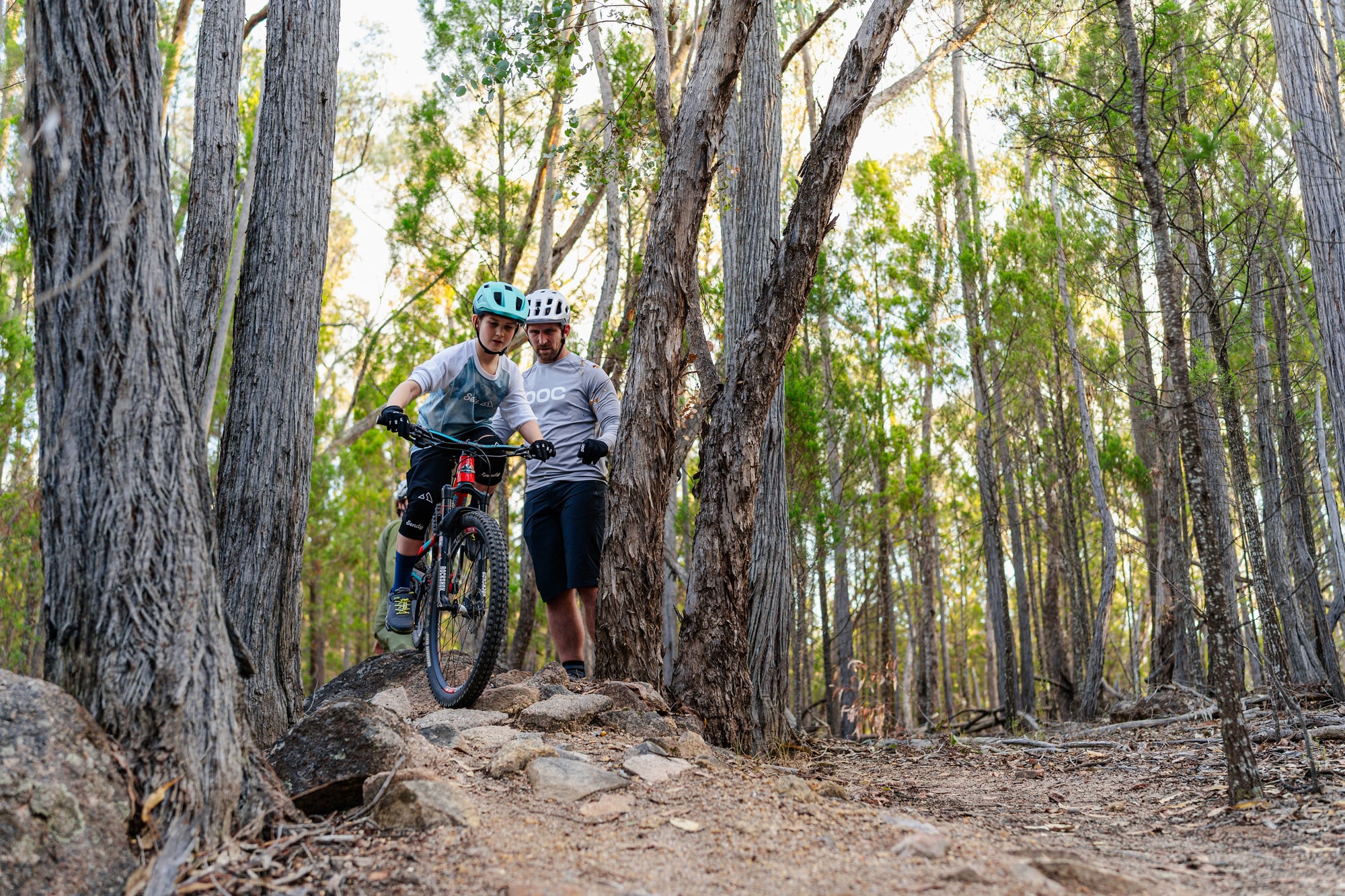 An adult mountain biker teaching a child mountain biker how to tackle Beechworth Mountain Bike Park's technical trails.