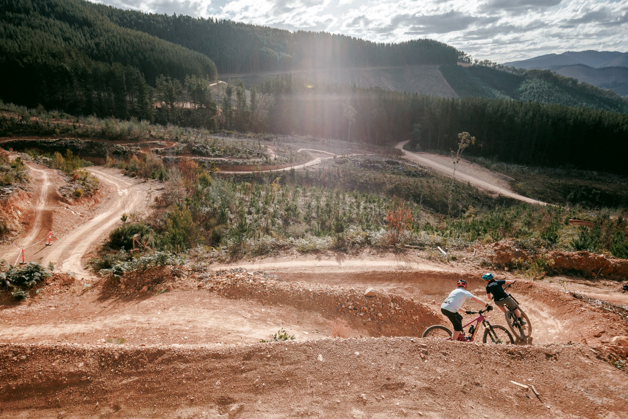 Two mountain bikers riding the berms at Mystic Bike Park with views of pine covered hills.