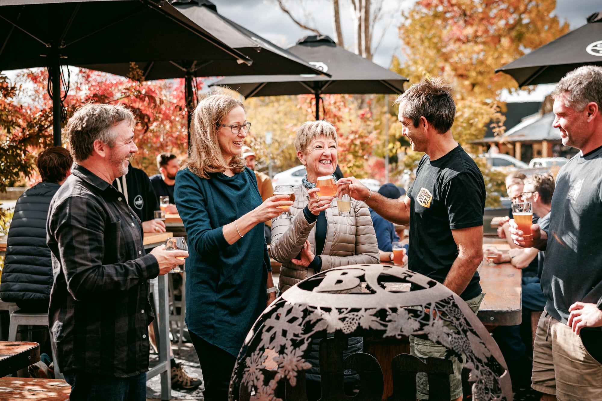 Group of people enjoying beers at Crank Handle Brewery around a fireplace with autumn leaves in the background