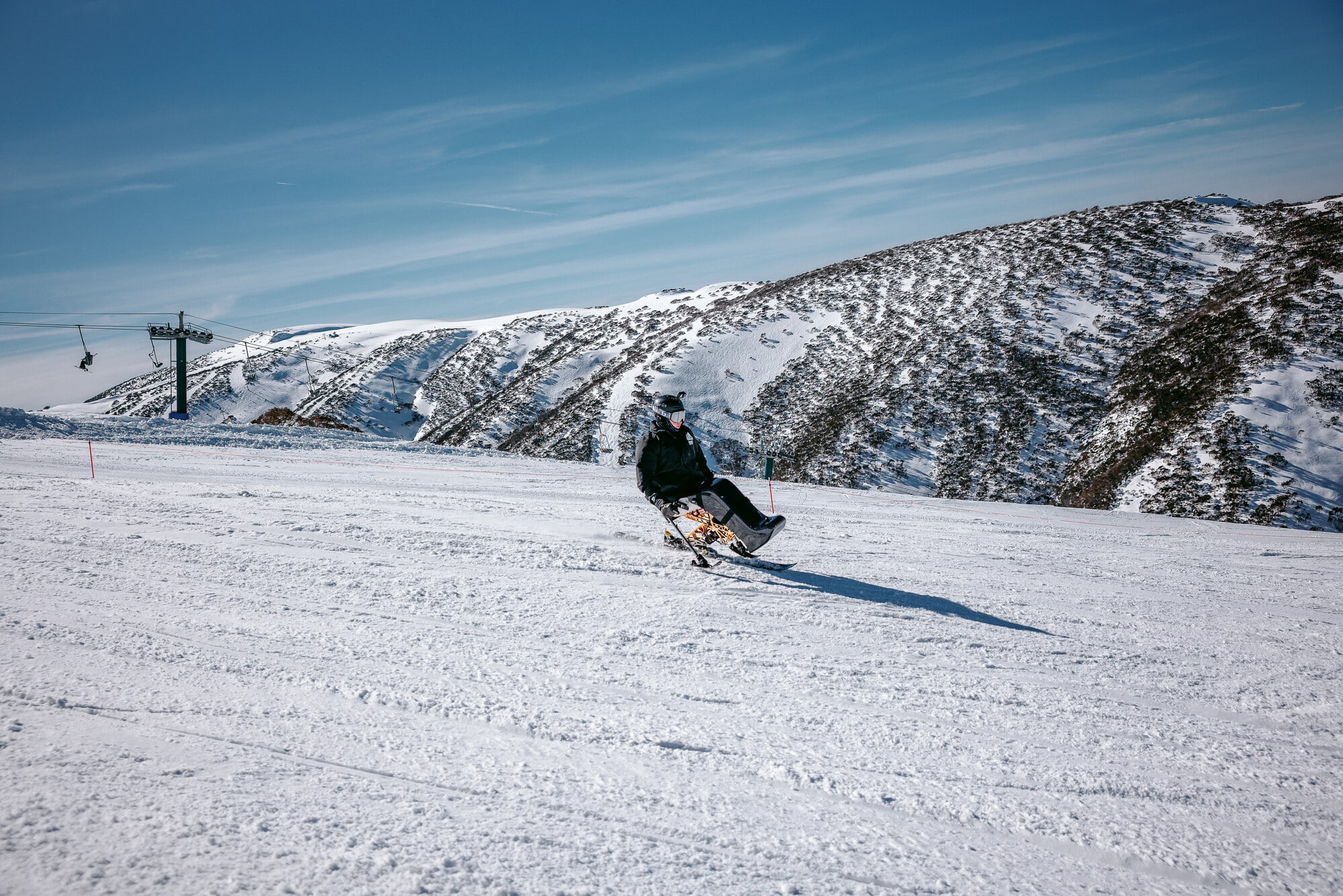 An adaptive skier skiing on the slopes of Mt Hotham with snow mountain views in the background.
