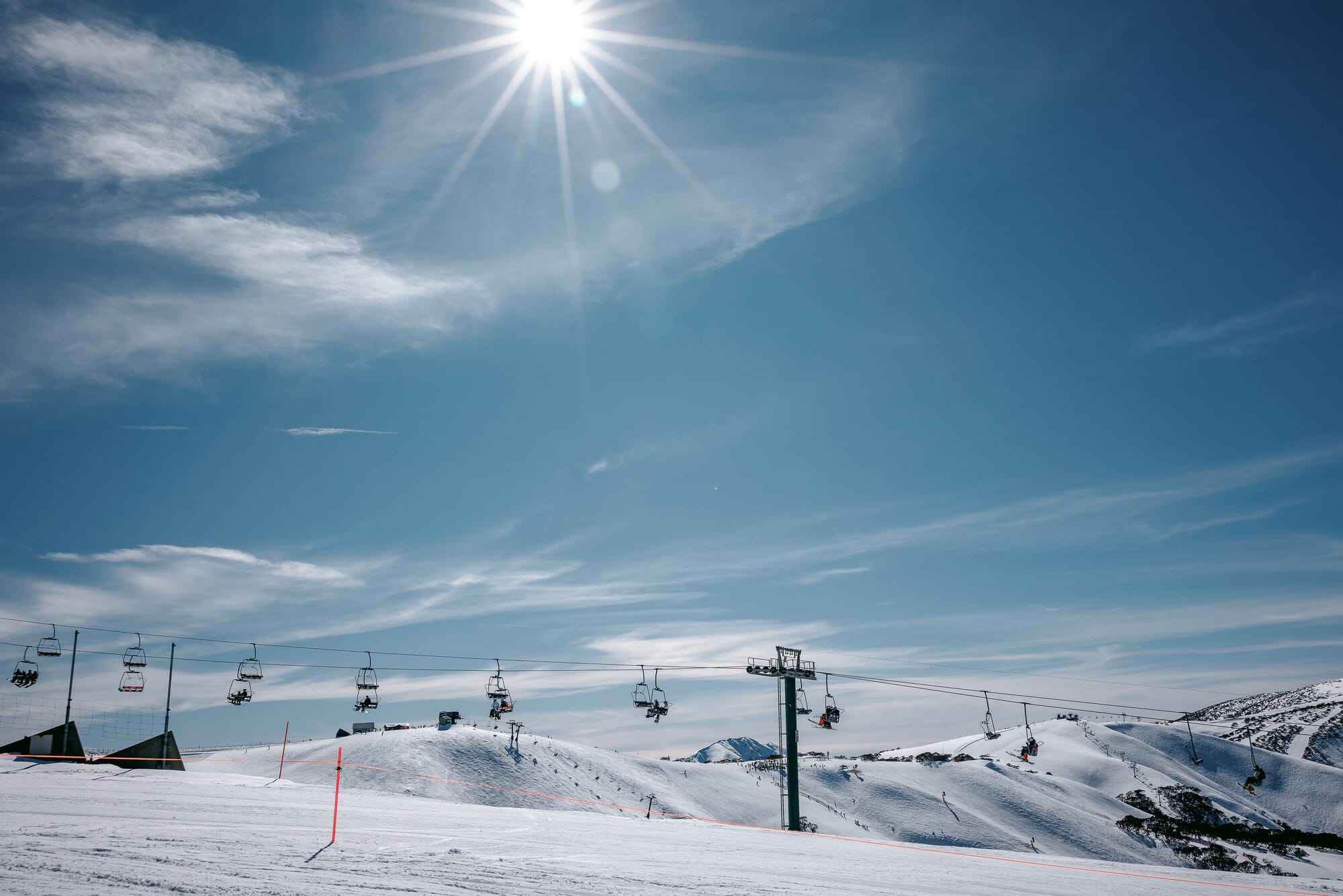 Chairlift at Mt Hotham on a sunny blue sky day with snowy mountain views in the background.