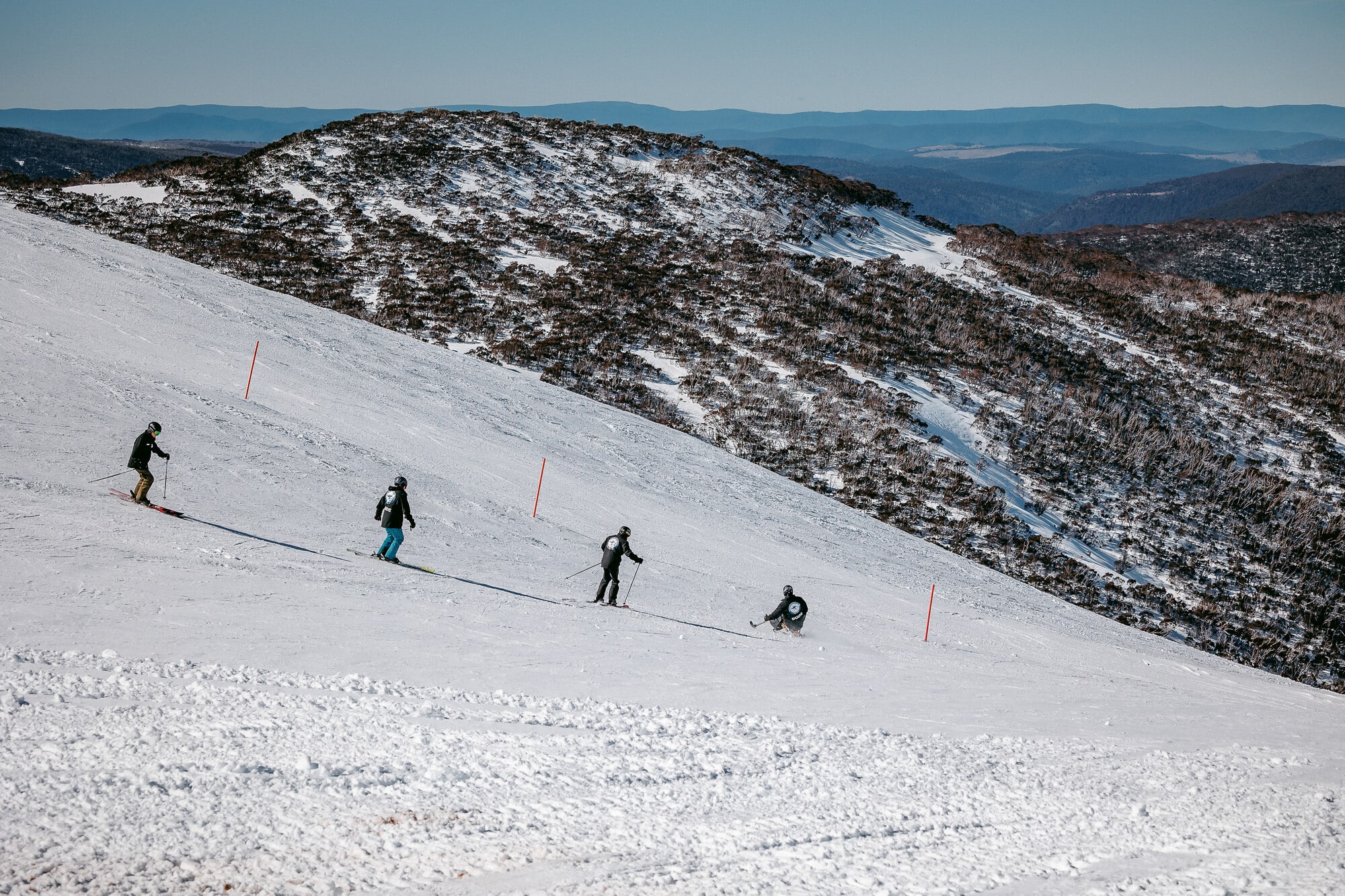 Adaptive skier and Disabled Wintersport Australia guide skiing on Mt Hotham's slopes with views of the mountains in the background.