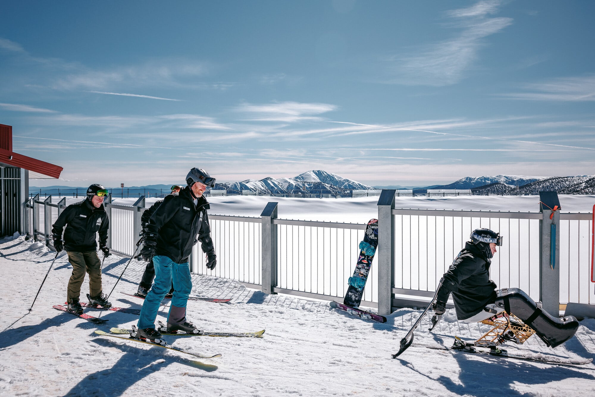 Adaptive skier with Disabled Wintersport Australia guides skiing from the Alpine Gateway Hub at Mt Hotham with snowy mountain views in the background.