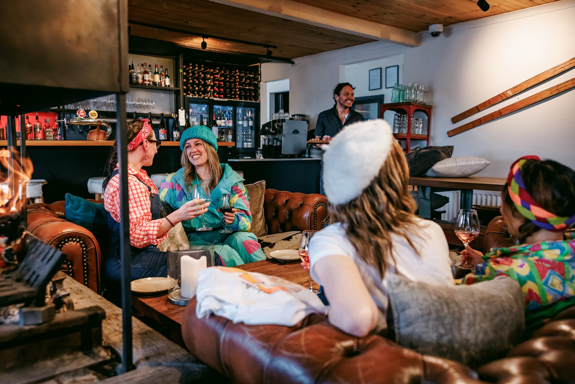 Group of people in vintage snow wear enjoying fireside drinks and charcuterie at Feathertop Alpine Lodge at Falls Creek.