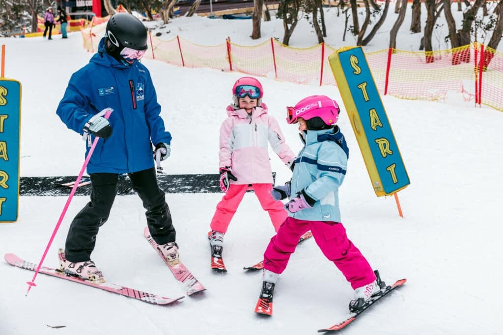 Two children dressed in warm winter clothes with a Mt Buller Ski and Snowboard School instructor participating in a ski lesson.