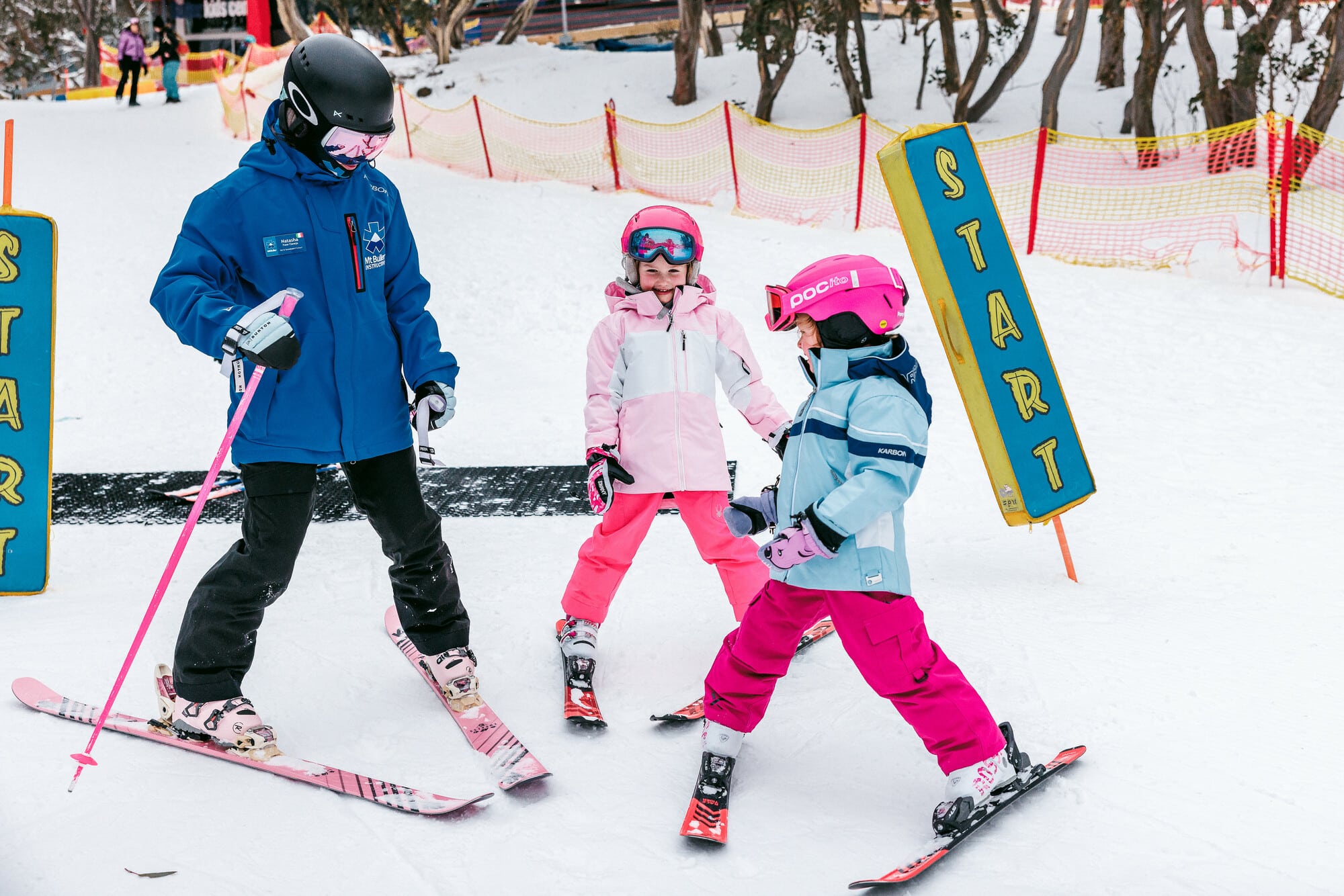 Two children dressed in warm winter clothes with a Mt Buller Ski and Snowboard School instructor participating in a ski lesson.