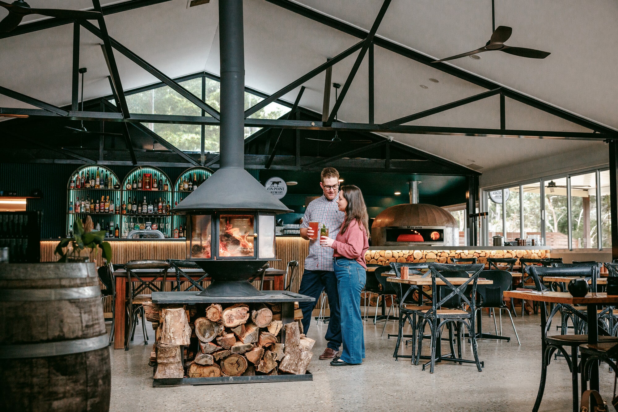 Two people standing by a fireplace with drinks at Lake Eildon Hotel with the bar in the background.