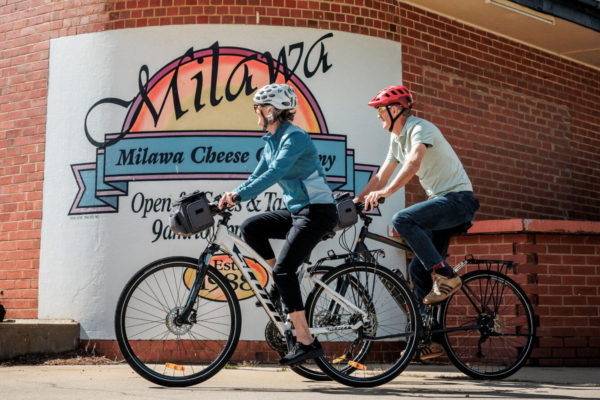 Two cyclists pedalling past the Milawa Cheese Company sign in Milawa.