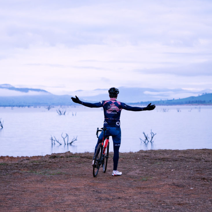 A gravel bike cyclist with arms out beside Lake Hume